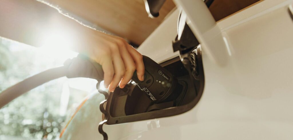 Main branchant un cable de recharge sur une voiture electrique blanche en cours de charge pour mobilite durable